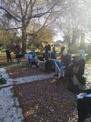 Members of the Friends of Southern Necropolis stand in the cemetery at lecterns in a row. The sun is behind them.
