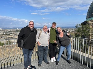 A group photo of 4 members of Invisible Cities posing against a city skyline with a blue sky