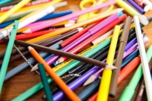 A closeup photo of a pile of coloured pencils. The photo is very saturated to emphasise the colourful paint on the pencils.