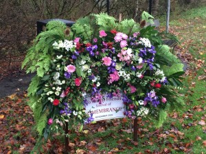 A photo of a public outdoor floral display with a sign reading "To Absent Friends - A Festival of Remembrance - November 2020".