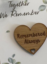 A photo of a wooden heart remembrance keepsake that says "Remembered Always" on a paper background.