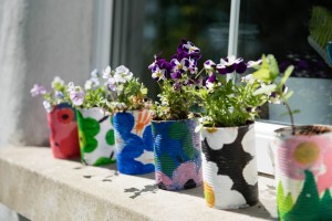 A photo of a windowsill full of painted coffee cans full of plants.